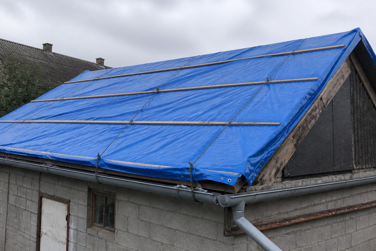blue roof tarp cover secured over a sloped industrial roof for extended weather protection