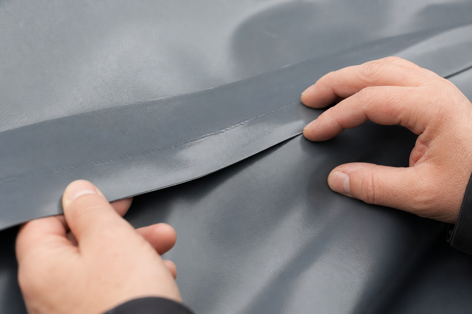 Technician inspecting a welded PVC tarp seam for overlap, fusion, and edge alignment before bulk production.