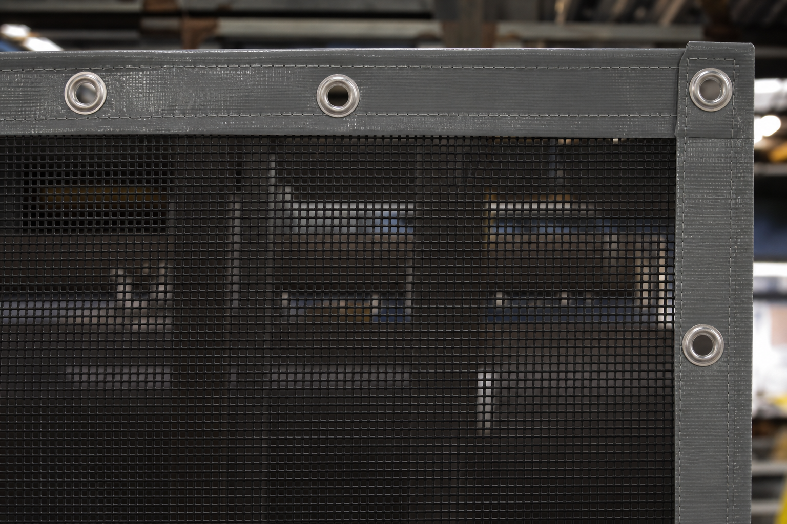 Reinforced edge and metal eyelet detail on a custom mesh tarp for industrial use