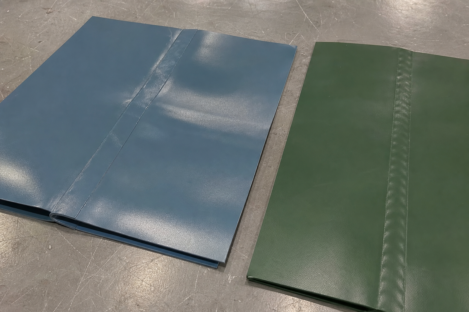 Two welded PVC tarp seam samples on a factory table for hot air and high frequency welding comparison