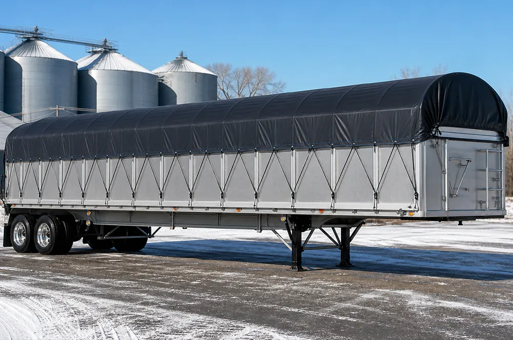 Reinforced black tarp system tensioned over a commercial cargo trailer in a cold-weather freight yard