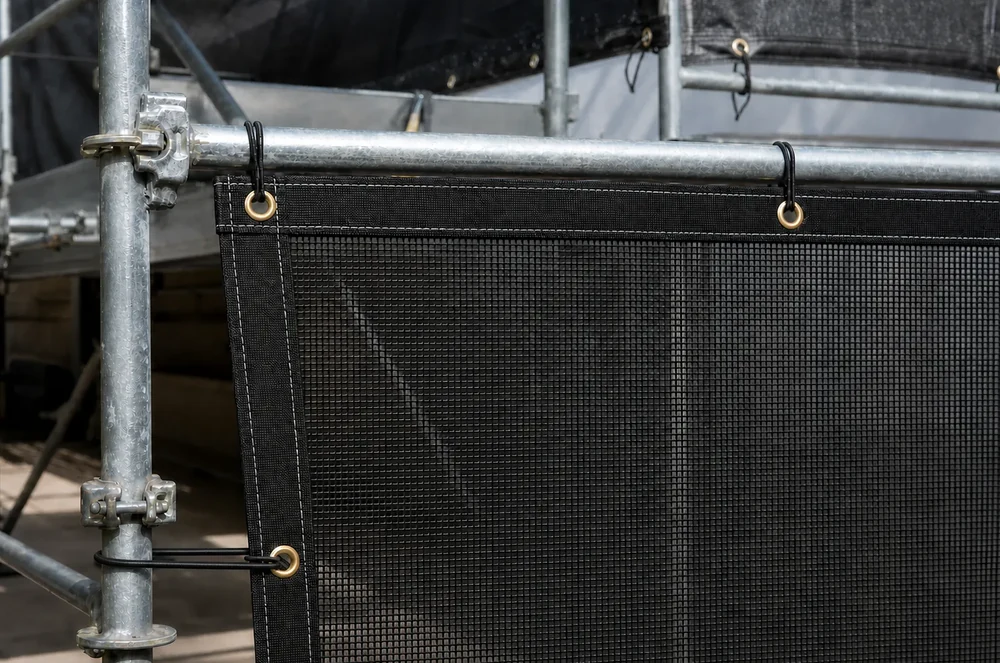 Black scaffold mesh tarp secured to scaffold tubes through reinforced eyelets