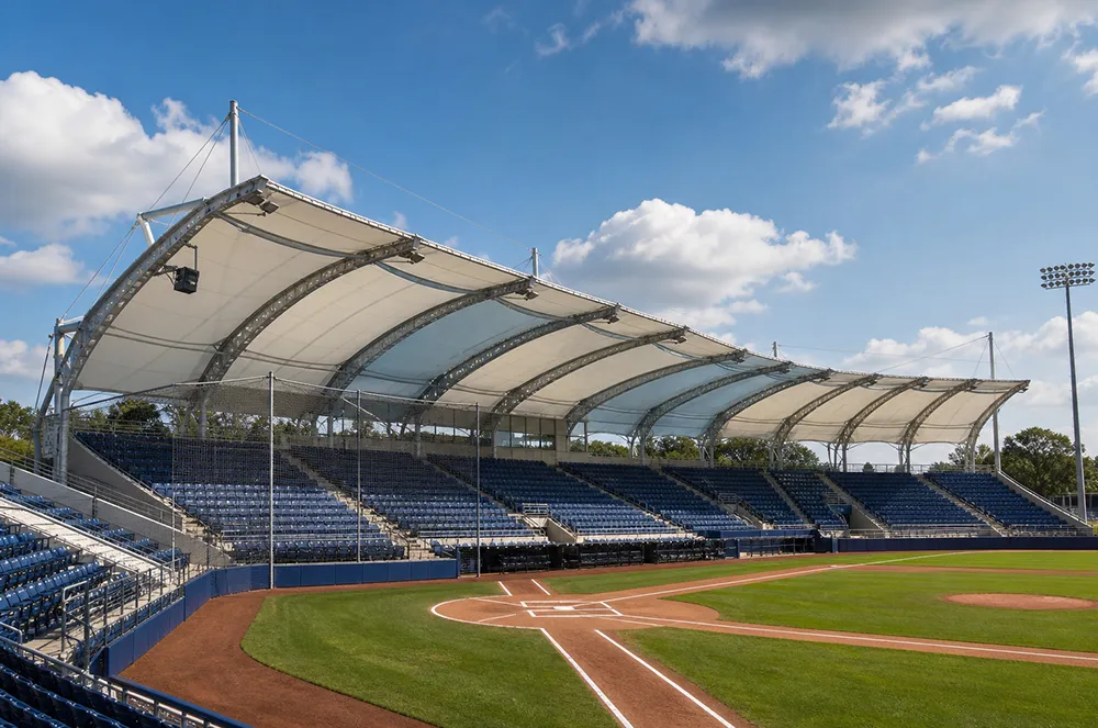 Membrane canopy protecting spectator seating at an outdoor baseball facility